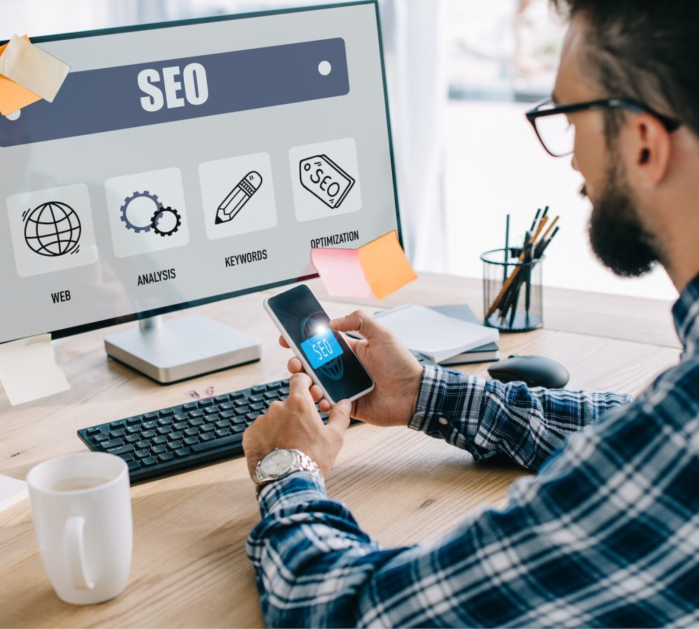 handsome young seo manager using smartphone and computer at workplace